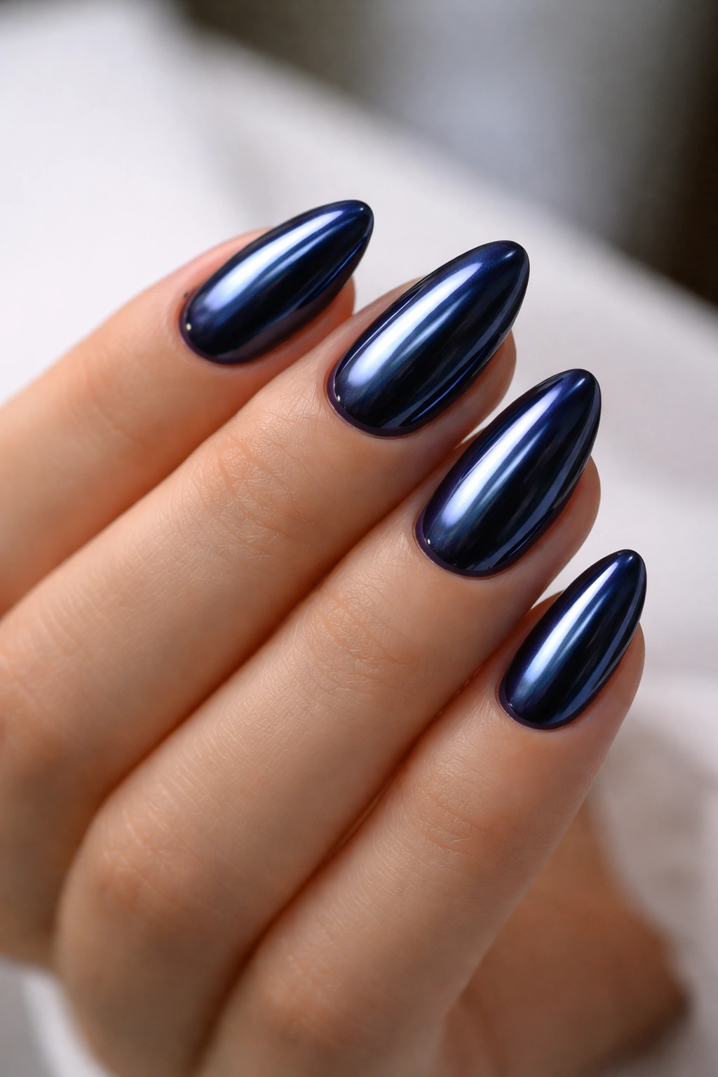 Short almond nails with navy chrome finish and reflective metallic surface.