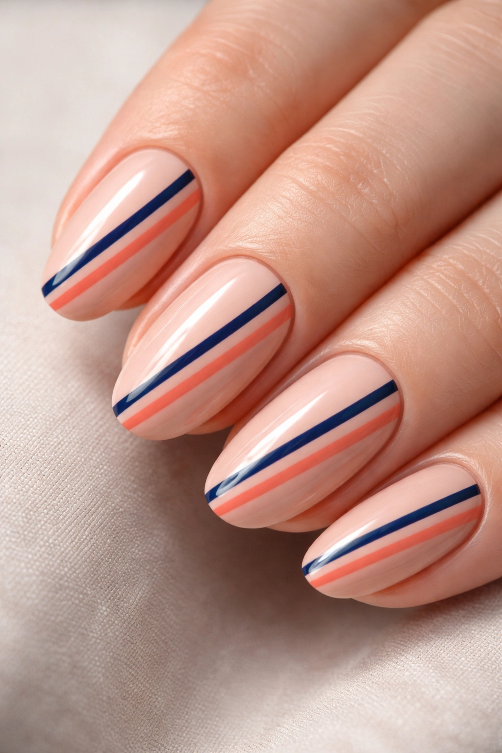 Close-up of nude nails with navy and coral striped pattern