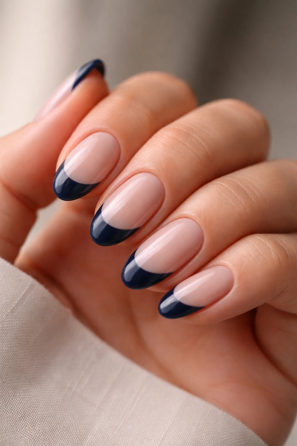 Close-up of a hand showing short almond nails with a navy French tip on a sheer nude base