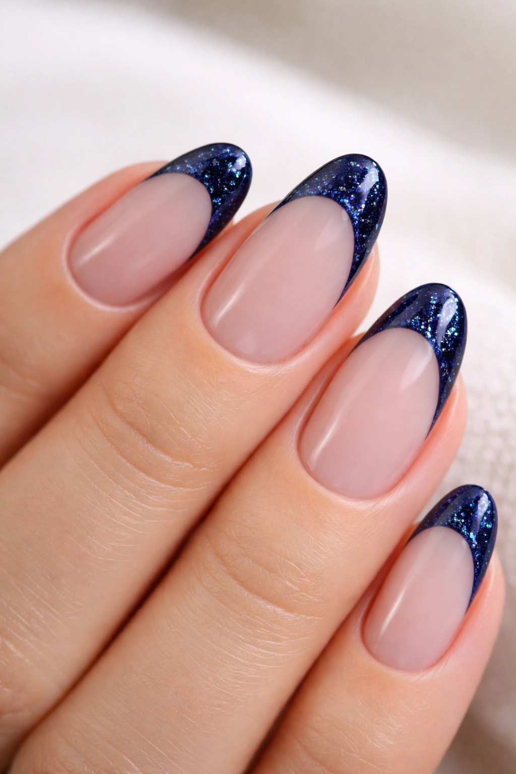 Close-up of short almond nails with navy tips featuring fine holographic glitter
