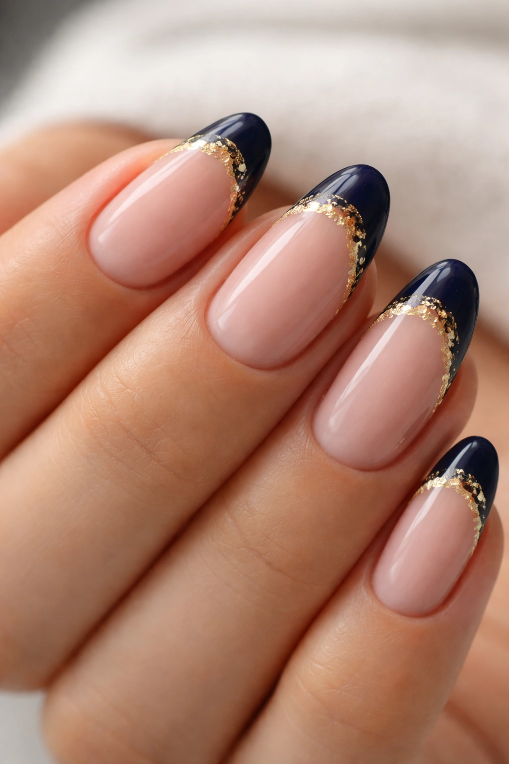 Close-up of short almond nails with navy tip and irregular gold foil along the smile line