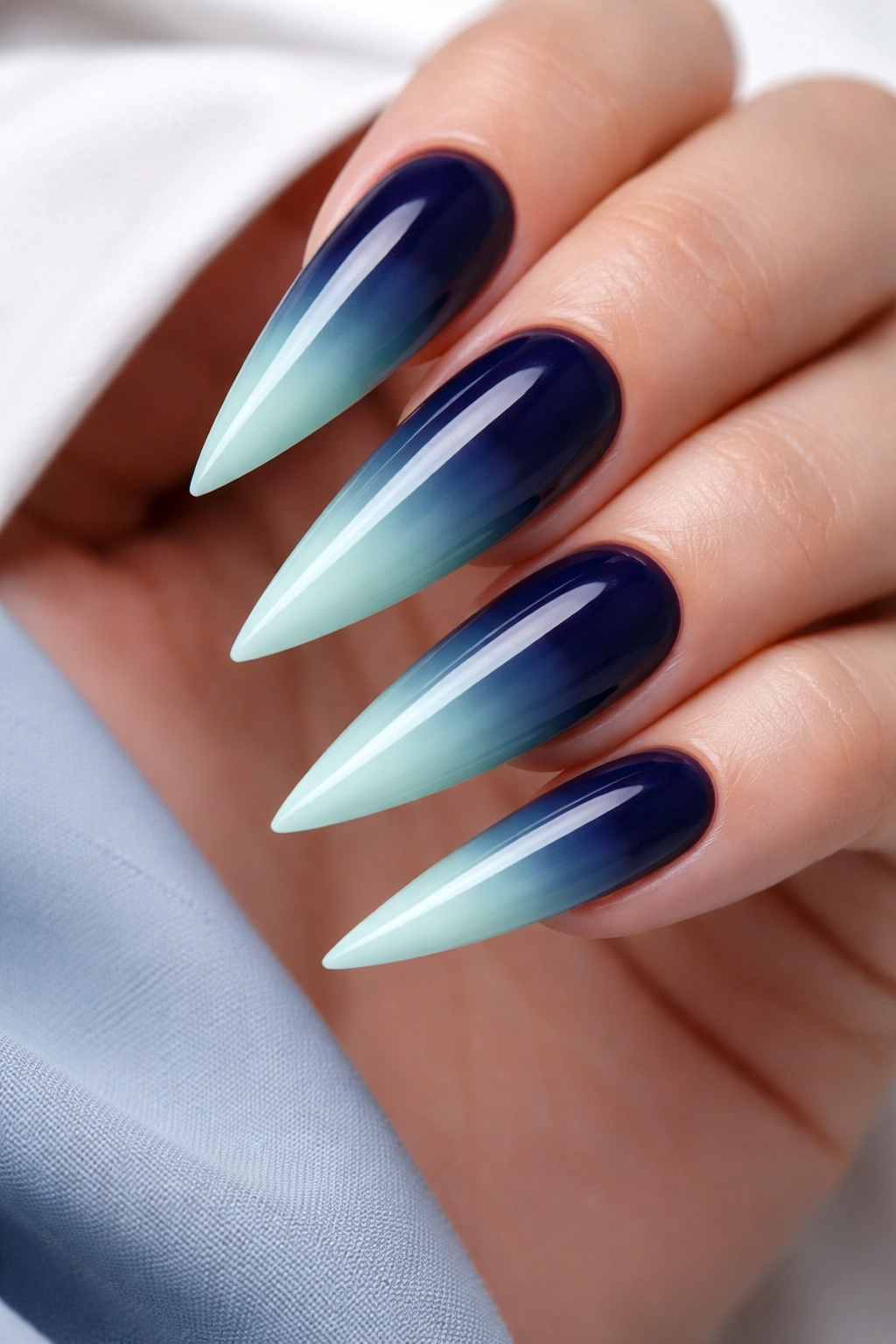 Close-up of stiletto nail with navy to mint green ombre in cool tones.