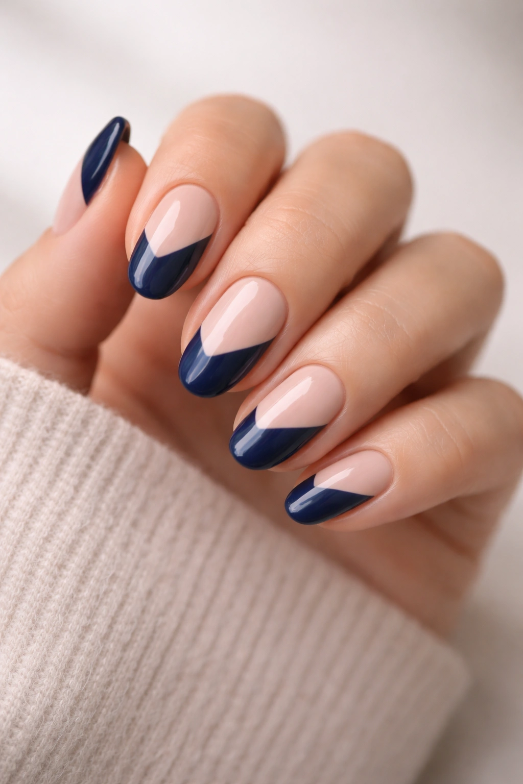 Close-up of short almond nails with diagonal navy blocks on a nude base.