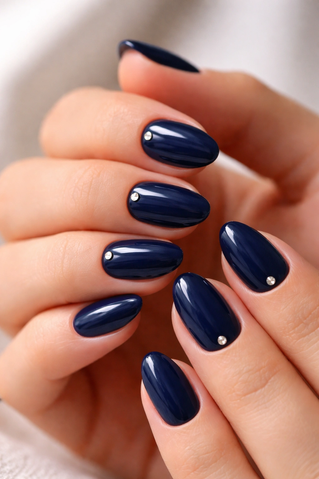 Close-up of navy almond nails with a single tiny crystal near the cuticle on each hand