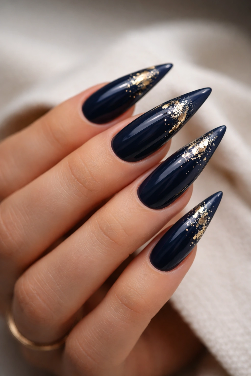 Close-up of deep navy stiletto nails with gold foil accents on a hand