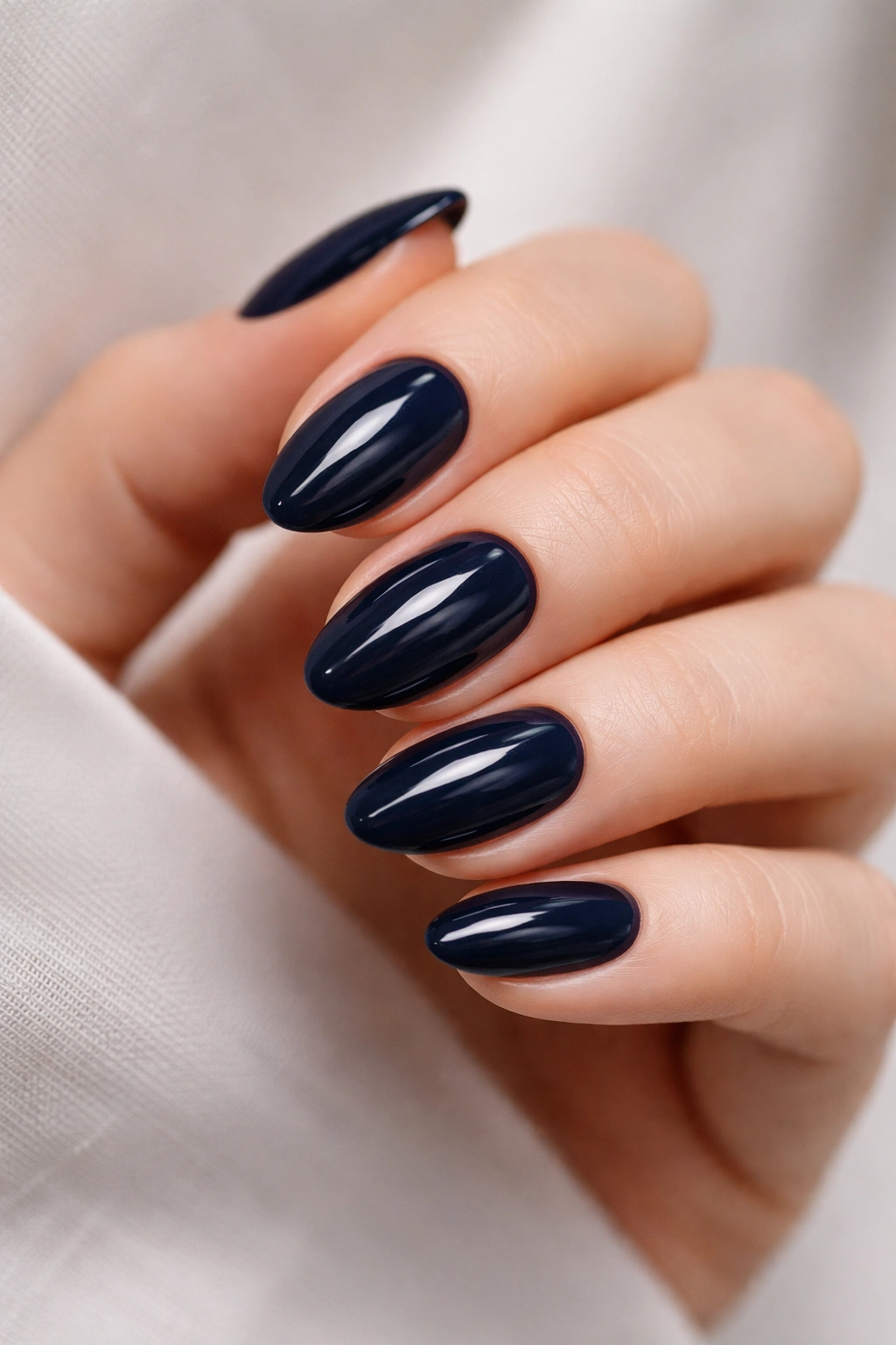 Close-up of short almond nails in deep navy with glossy finish
