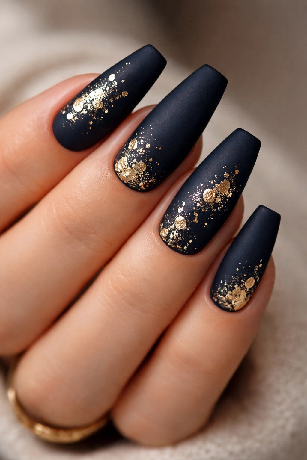 Close-up of deep navy coffin nails with gold leaf accents on a hand