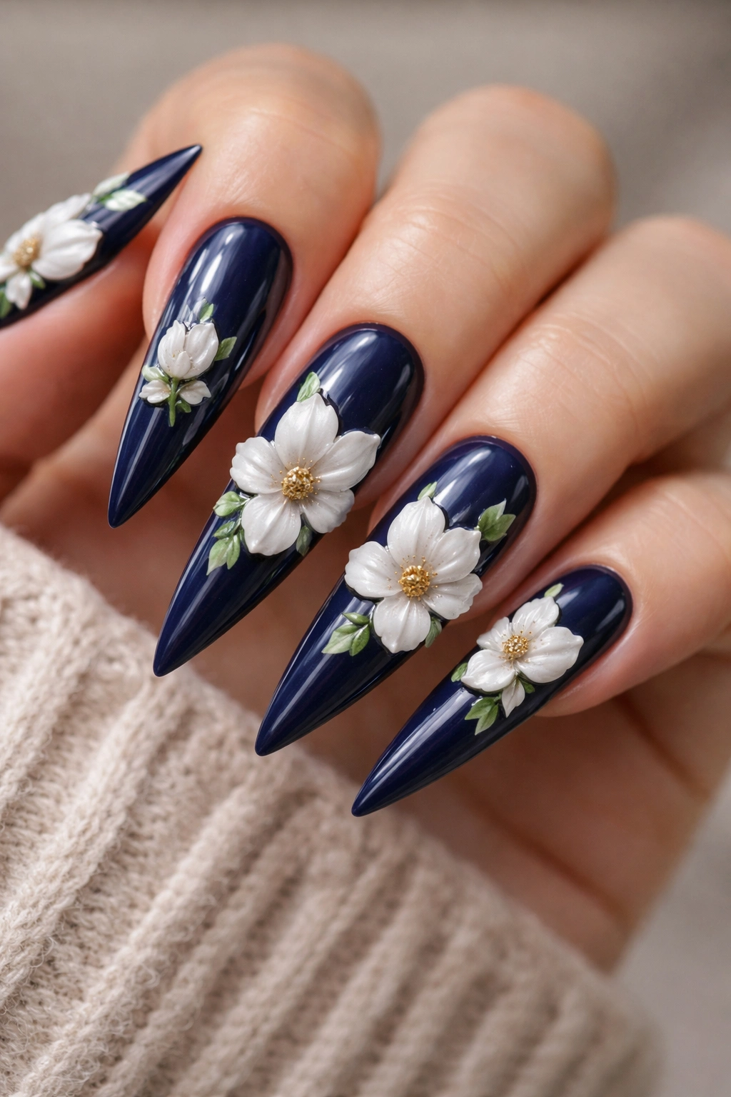 Close-up of navy stiletto nails with raised white magnolias and green leaves