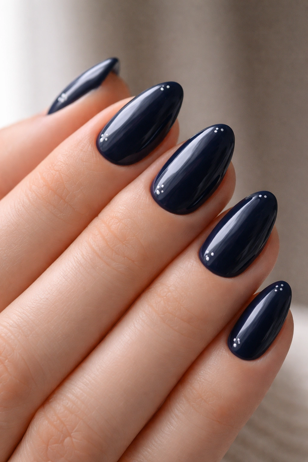Navy nails with tiny white or silver dots on almond nails.