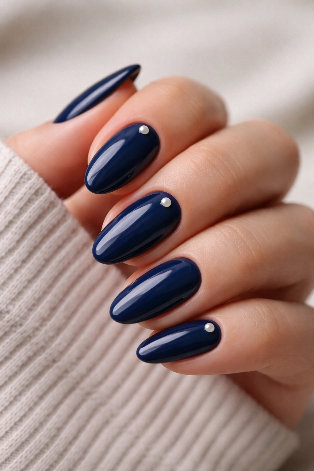 Navy nails with tiny pearl accents on a couple of almond nails, close-up.