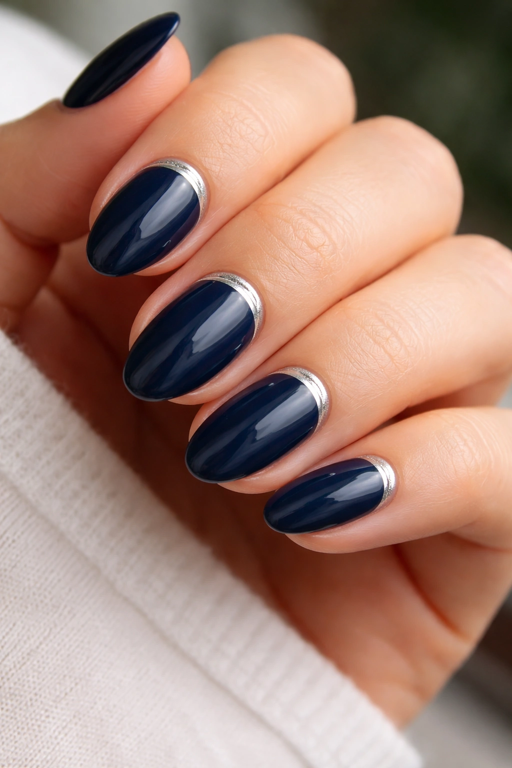 Close-up of navy almond nails with a thin silver crescent at the cuticle
