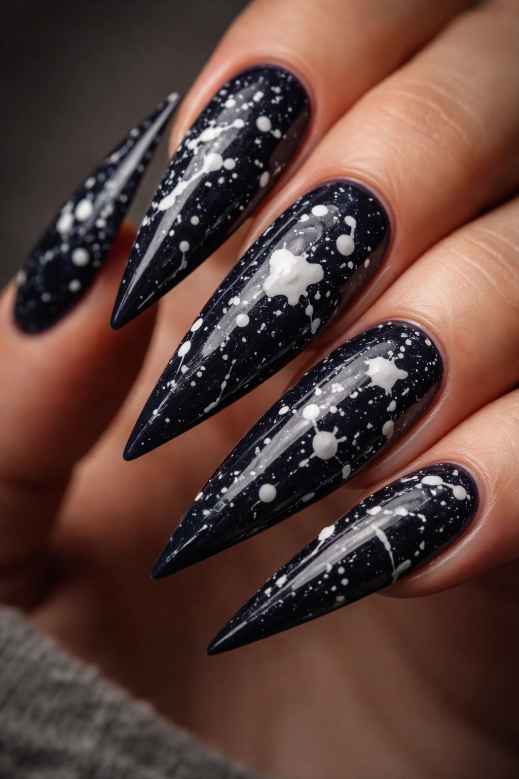 Close-up of dark navy stiletto nails with random white splatters on a neutral background.