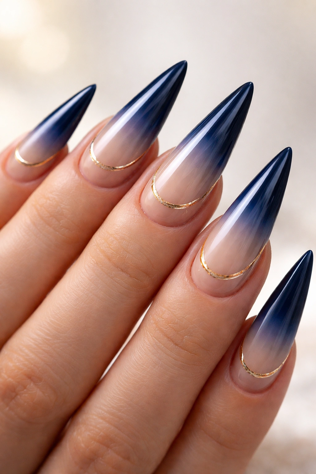 Close-up of navy to nude ombre stiletto nails with gold details near cuticle