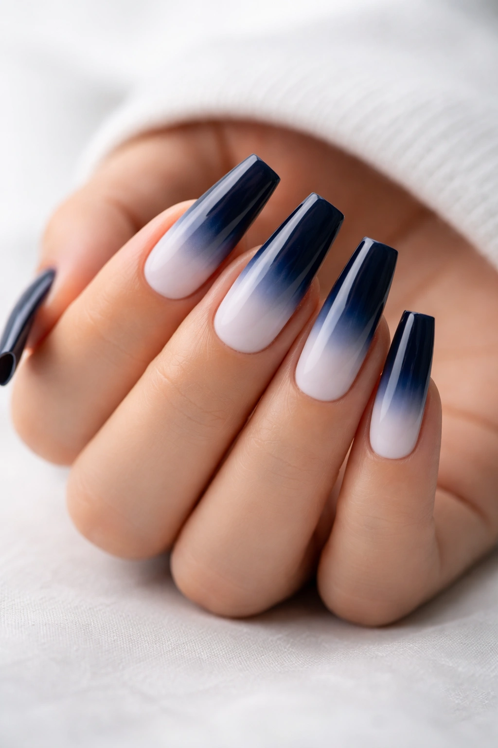Close-up of coffin nails with navy to white ombre gradient on a hand.