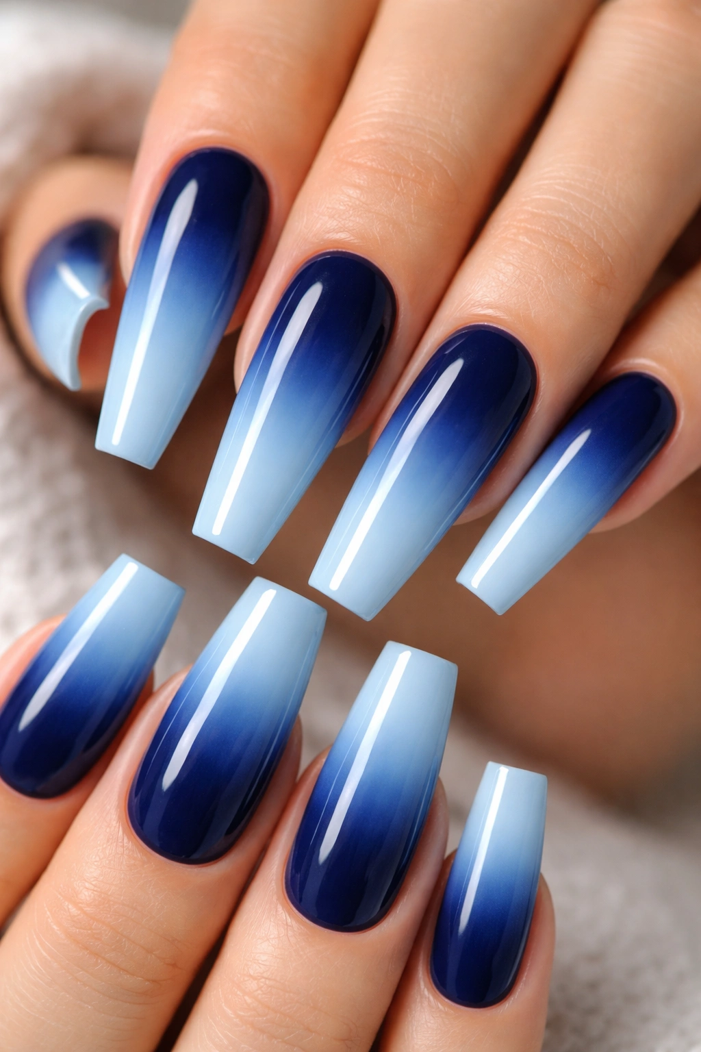 Close-up of long coffin nails in navy to sky blue ombre on a neutral background
