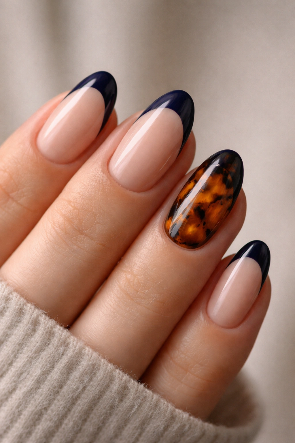 Close-up of a hand with navy tips on four nails and a tortoiseshell accent nail on the ring finger