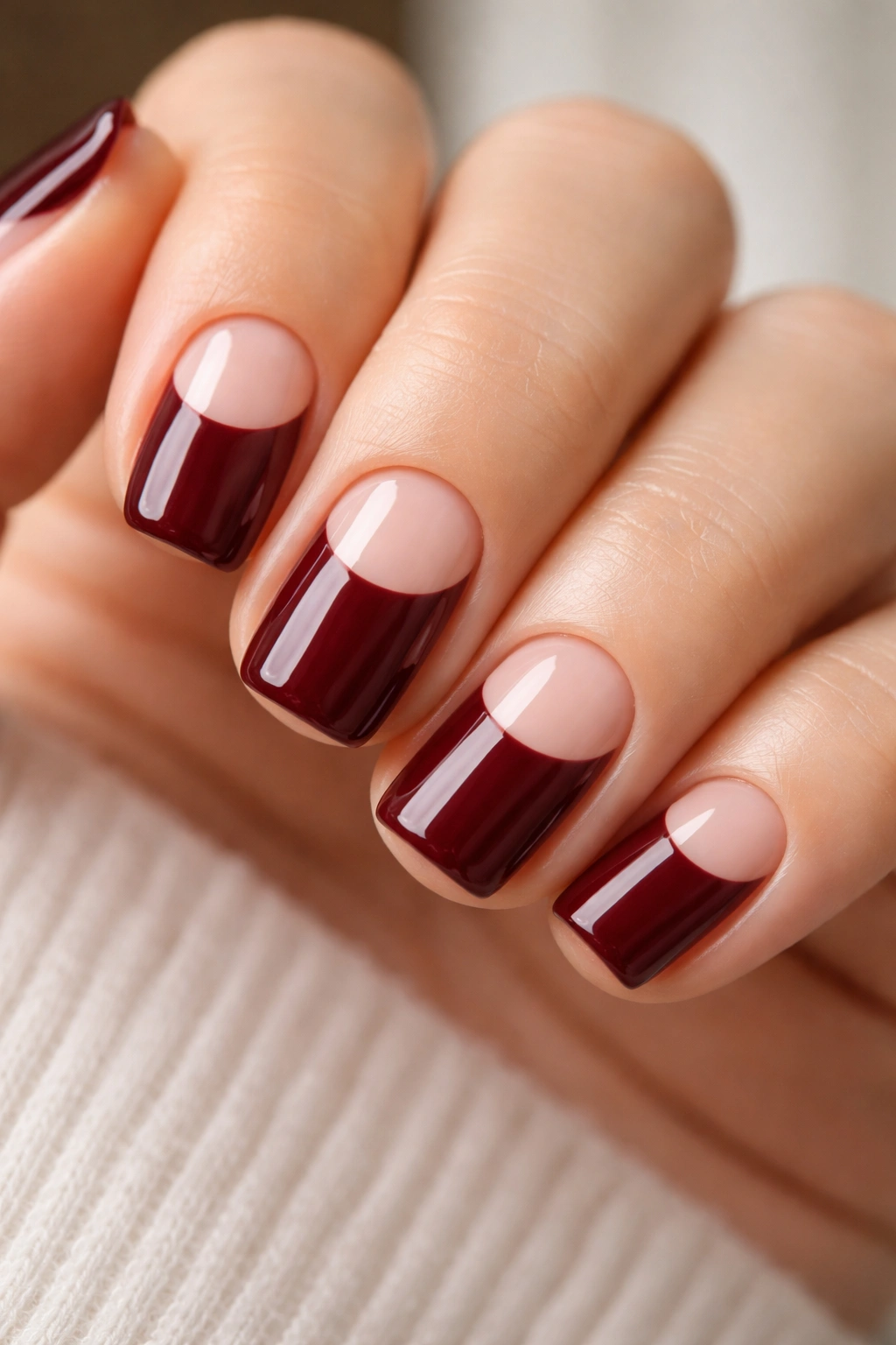 Short squoval nails with burgundy polish and deliberate negative-space design.