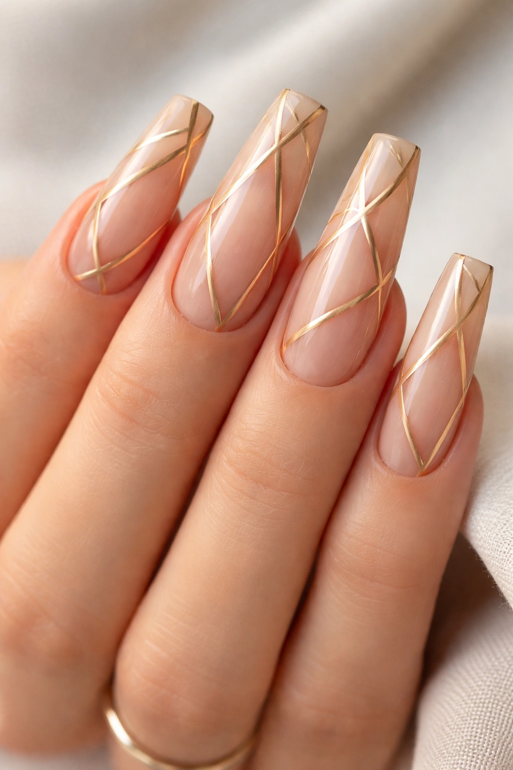 Nude curved coffin nails with thin gold geometric lines and negative space