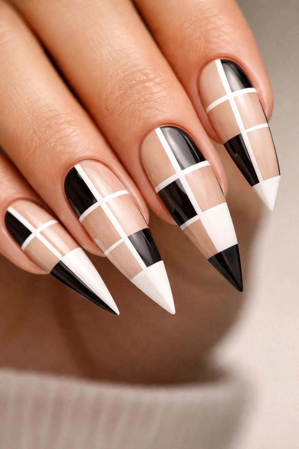 Close-up of reverse stiletto nails with a negative-space grid in black white and nude