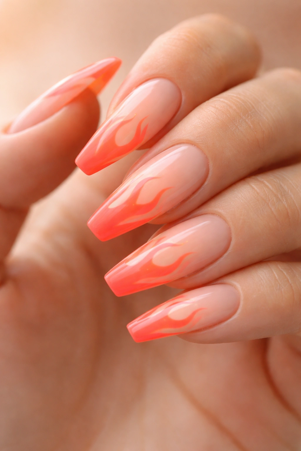 Close-up of neon coral flame tips on a soft peach base ballerina nails.