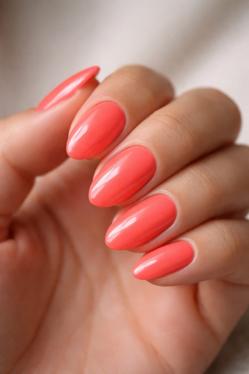 Close-up of neon coral nails on a glossy short almond base