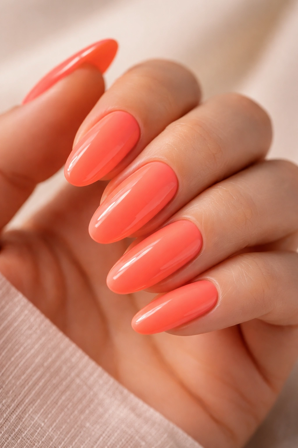 Close-up of long oval neon coral nails with a glossy finish on a neutral background