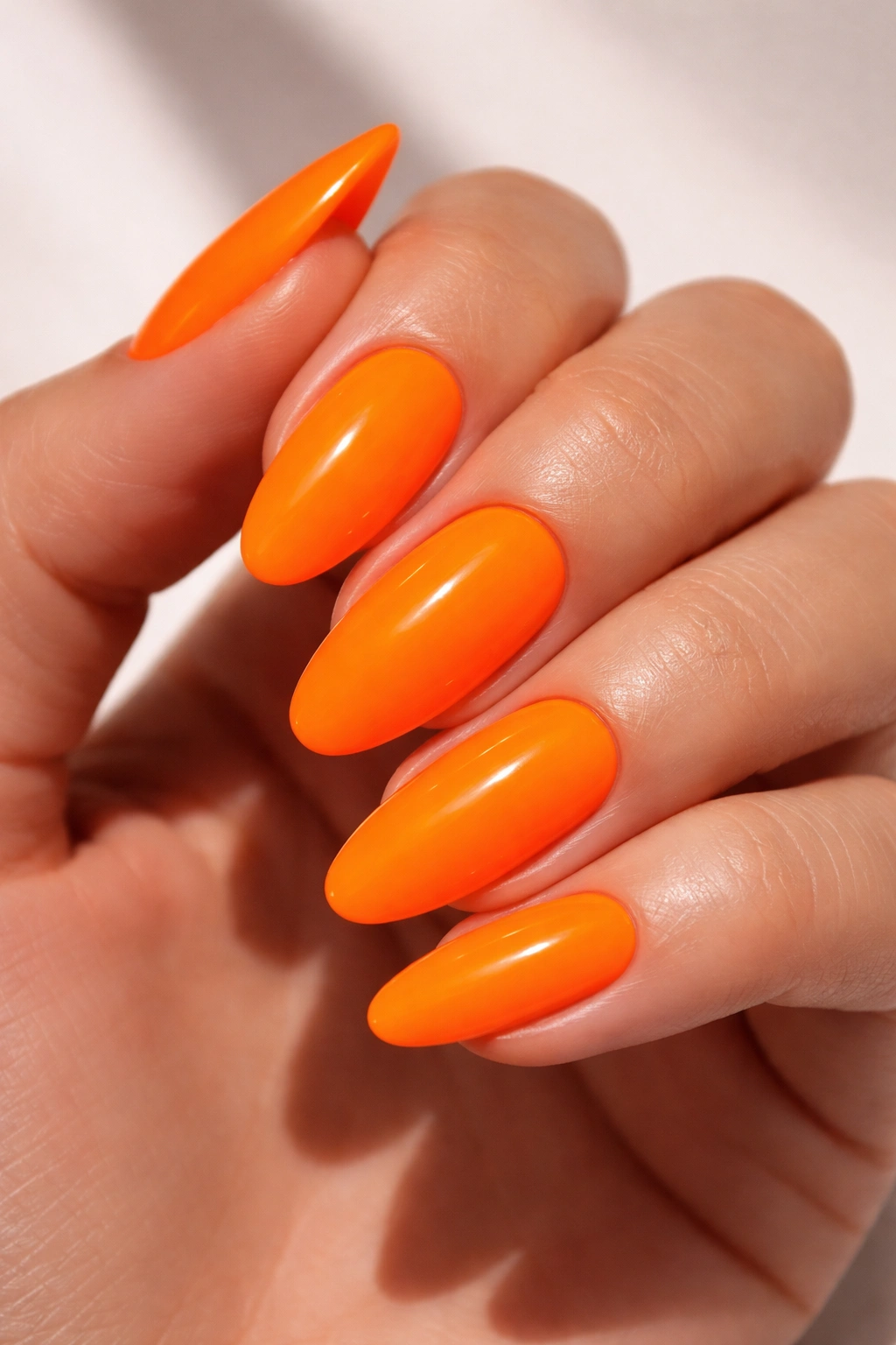 Close-up of neon orange nails glowing under bright light
