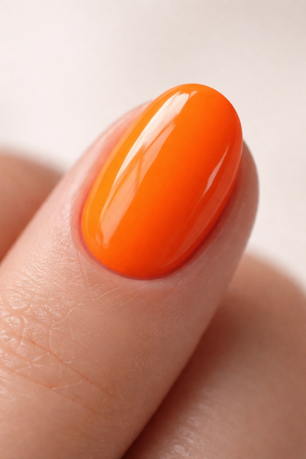 Close-up of a single neon orange short oval nail with glossy finish on neutral background