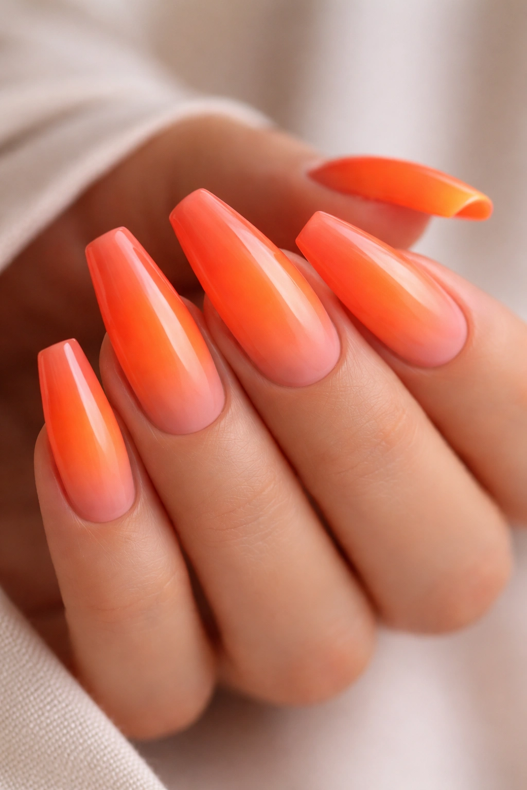 Close-up of neon orange ombre coffin nails on medium-length nails with a neutral background