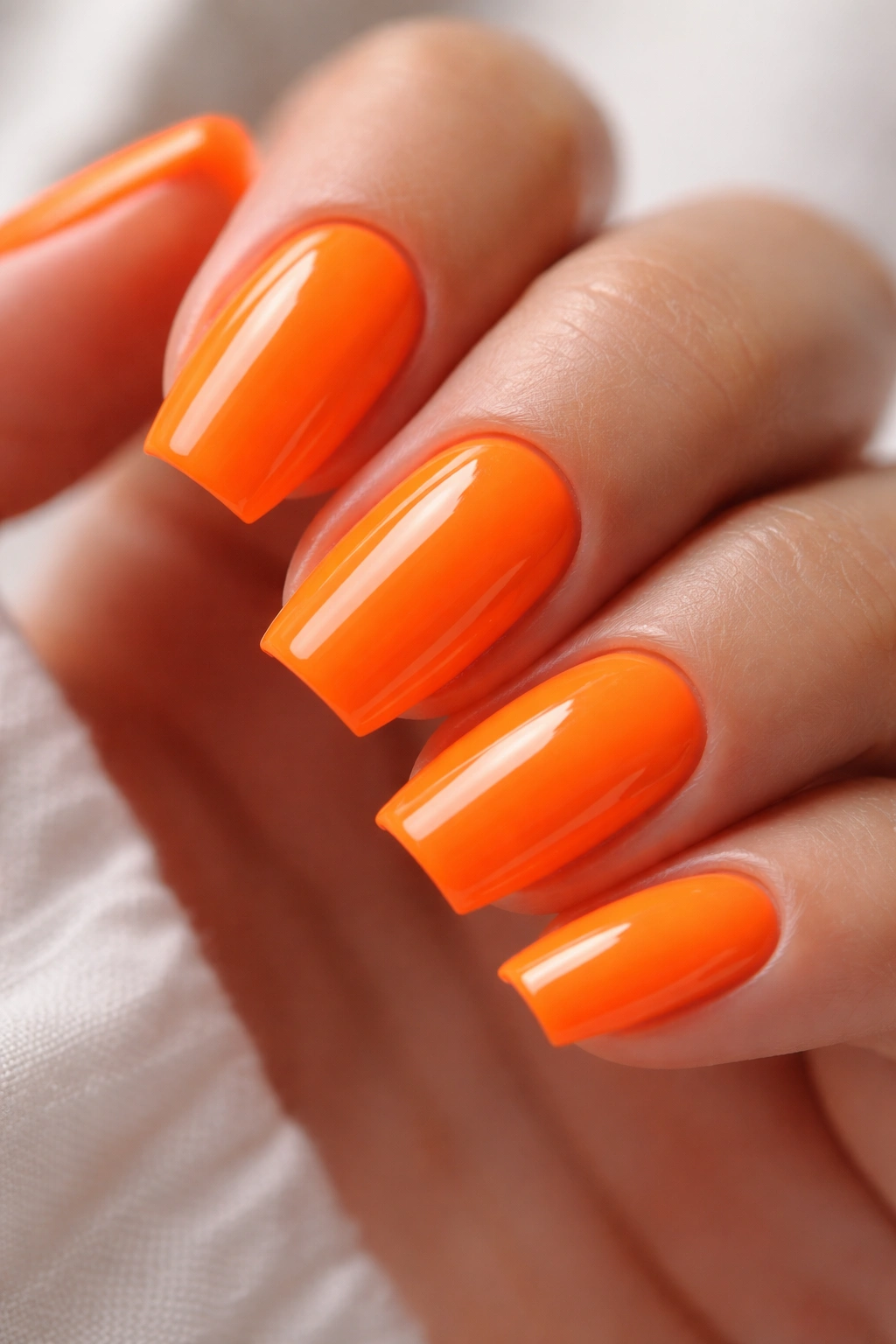 Close-up of short almond nails in neon orange with squared-off edge