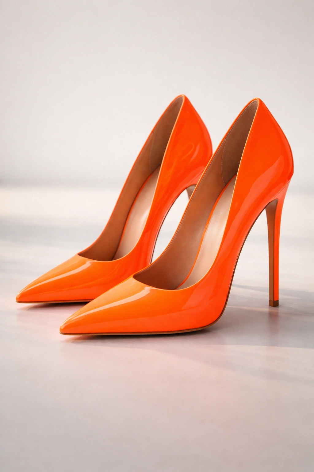Close-up of neon orange stilettos with glossy finish on white background
