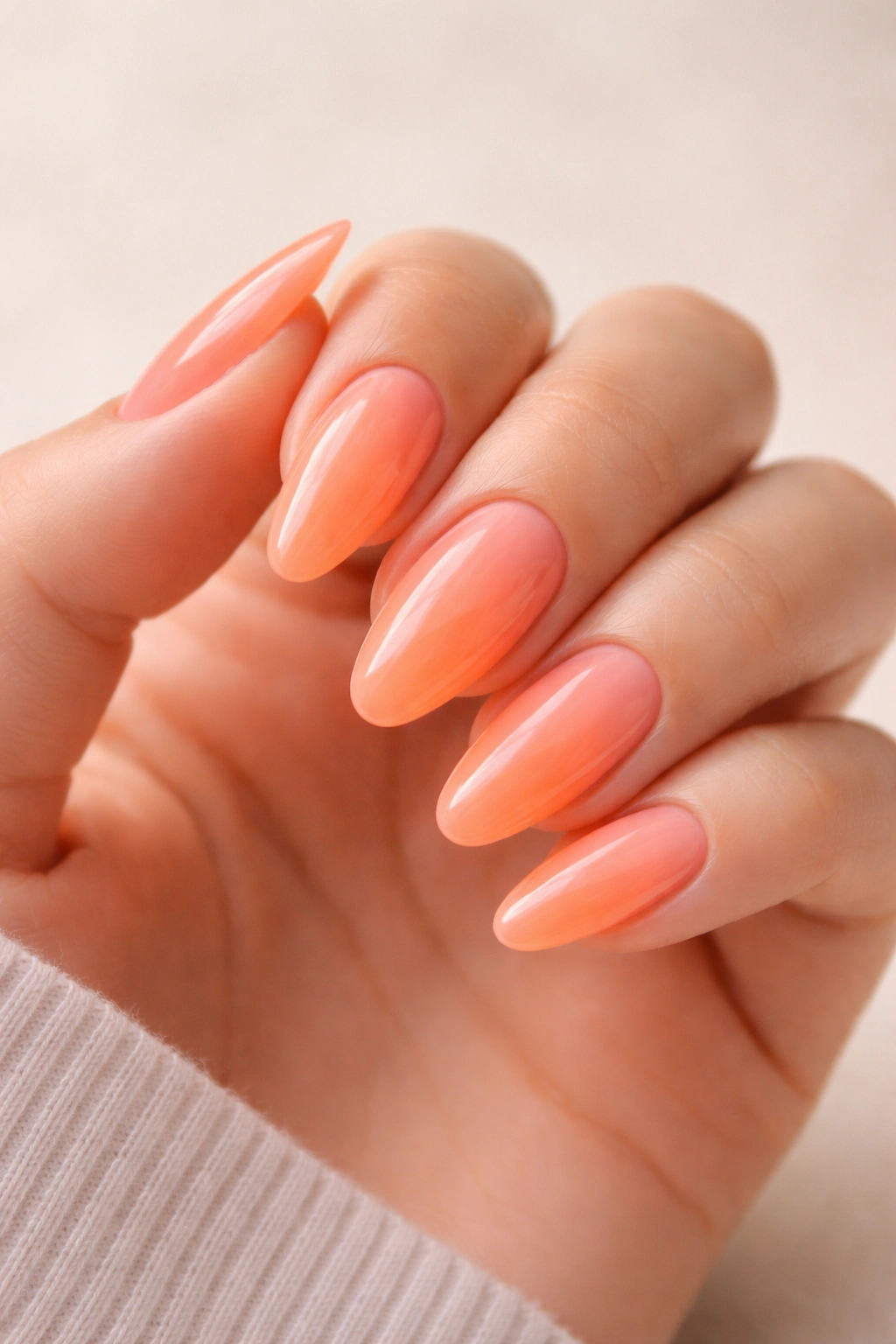 Close-up neon peach almond nails with jelly finish.