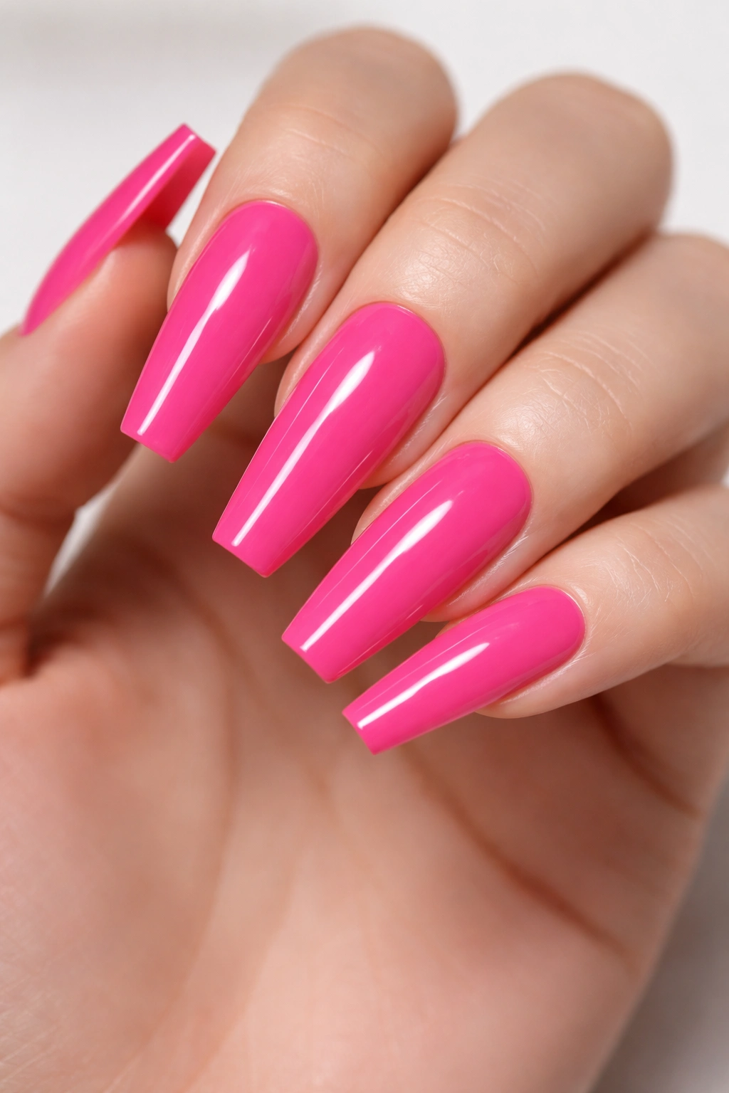 Neon pink coffin nails with sharp edges and high gloss on neutral background