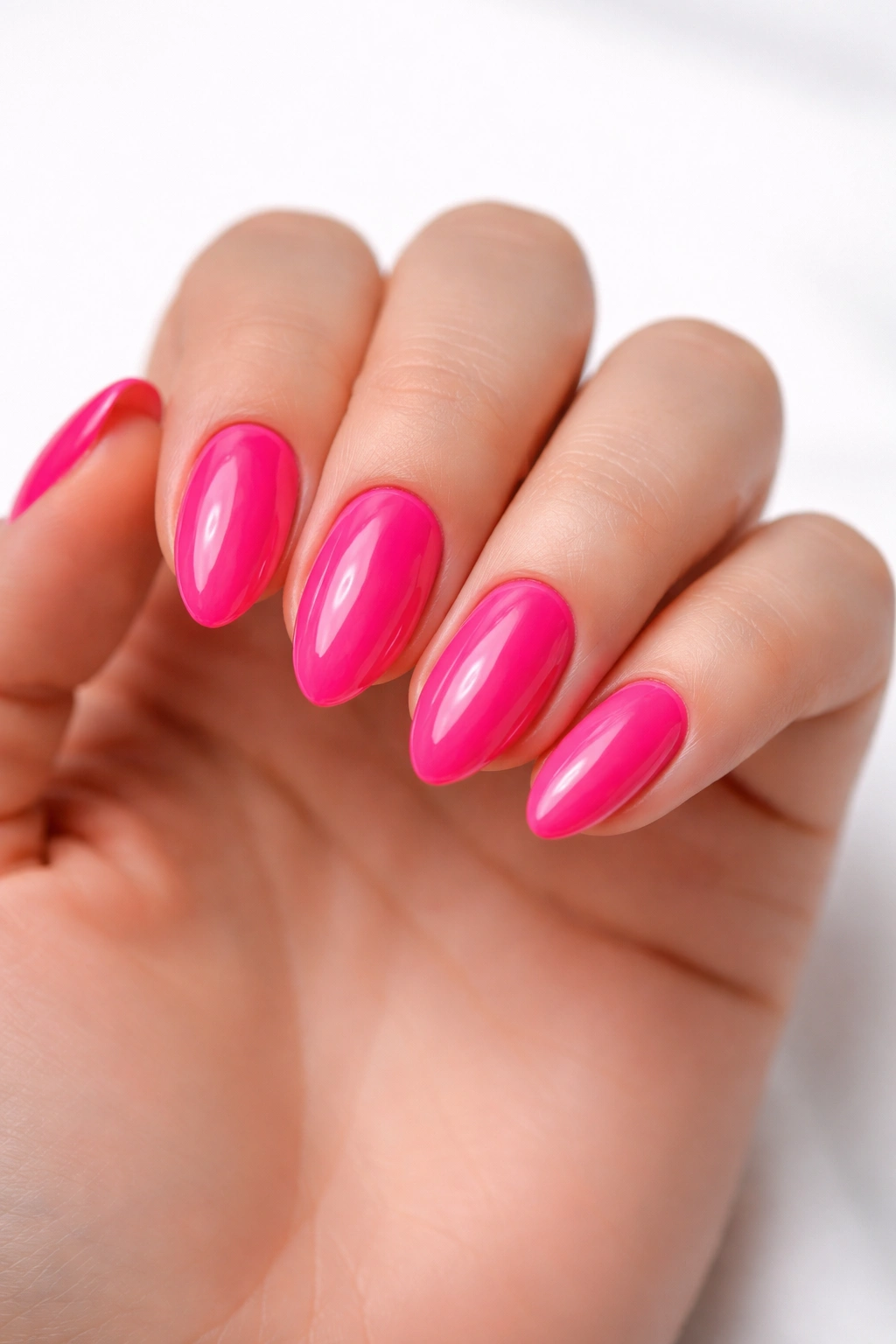 Close-up of glossy neon pink almond nails on a short manicure with a glassy finish