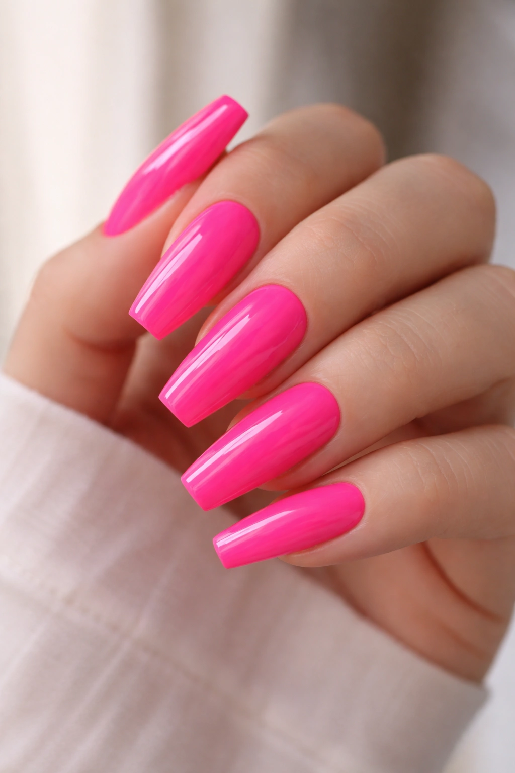 Close-up of a hand with medium coffin nails painted neon pink on a neutral backdrop