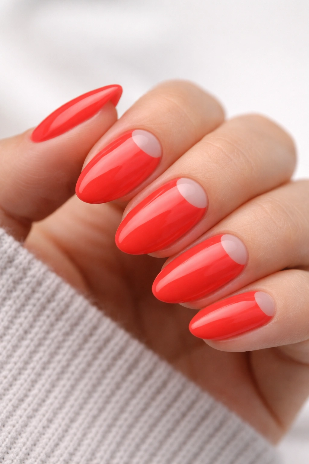 Close-up of a short almond neon red nail with a bare half-moon