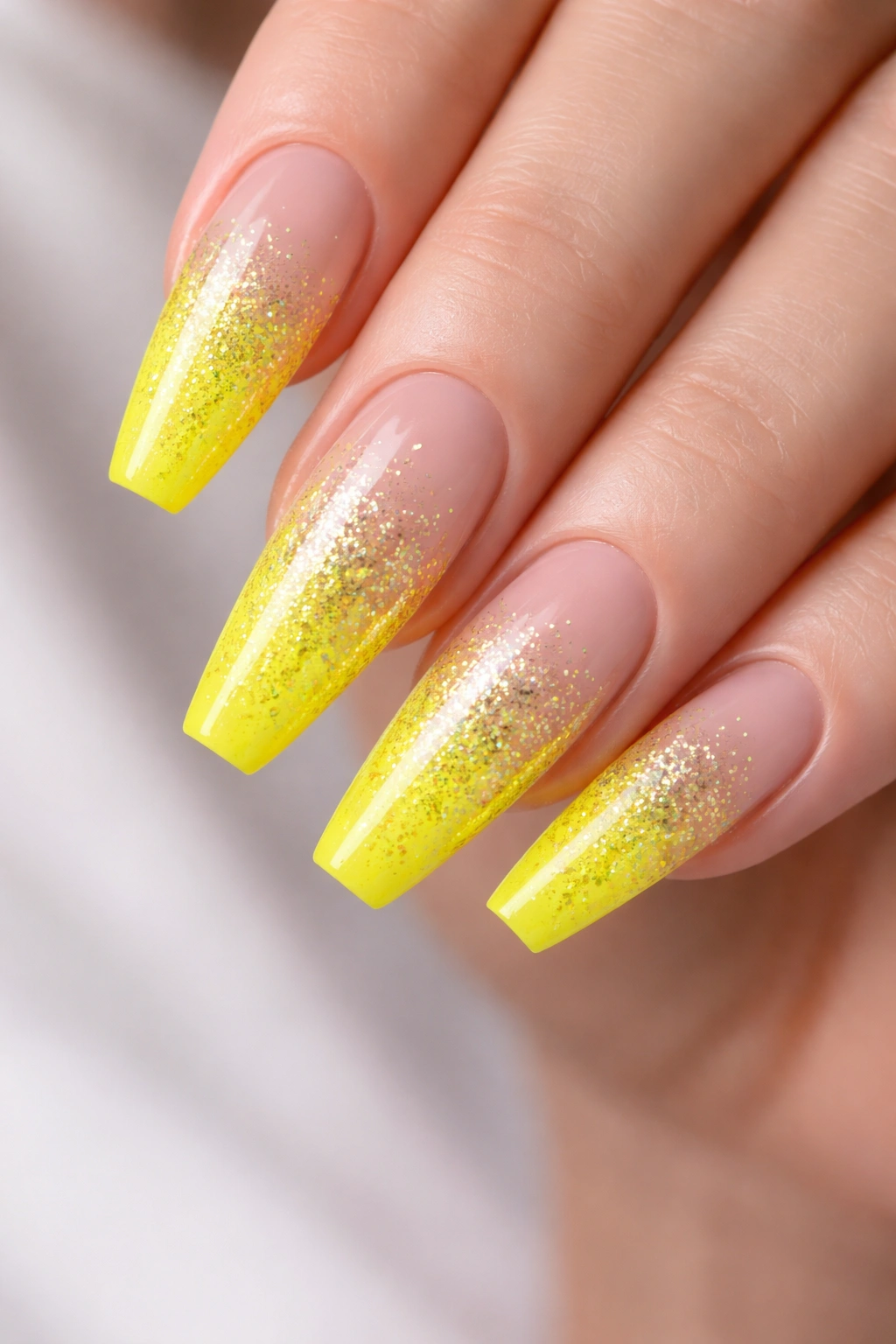 Close-up of neon yellow coffin nails with glitter ombré fading to clear