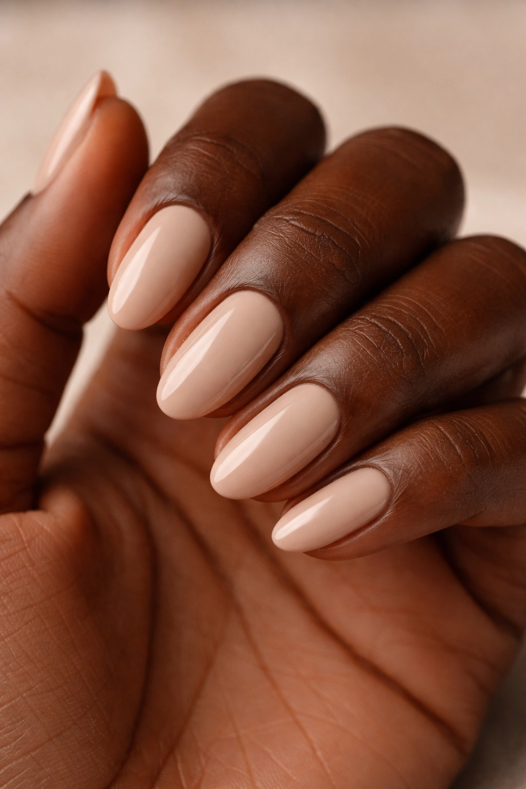 Close-up of neutral beige short almond nails on dark skin