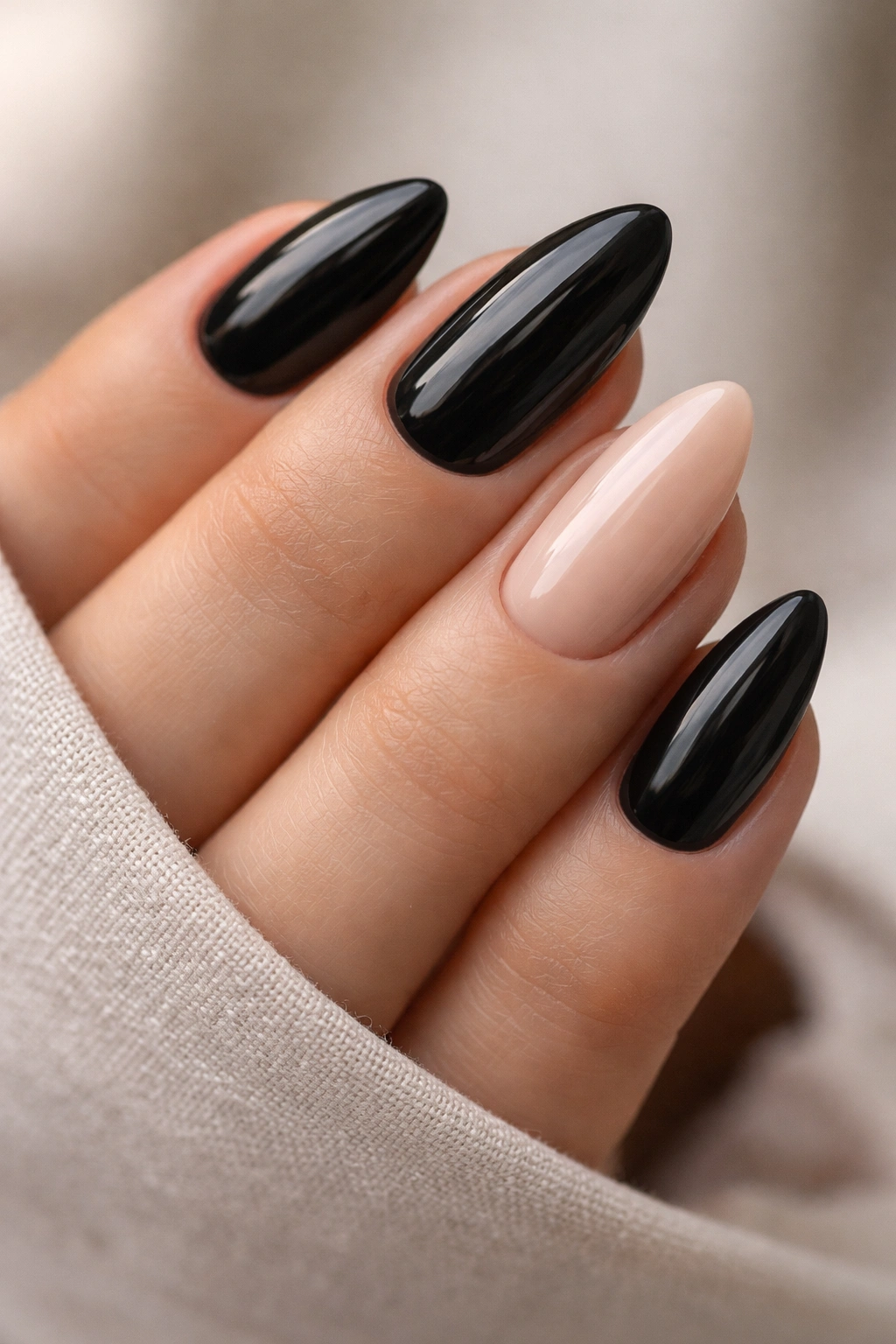 Close-up of black almond nails with a single nude accent nail on one finger