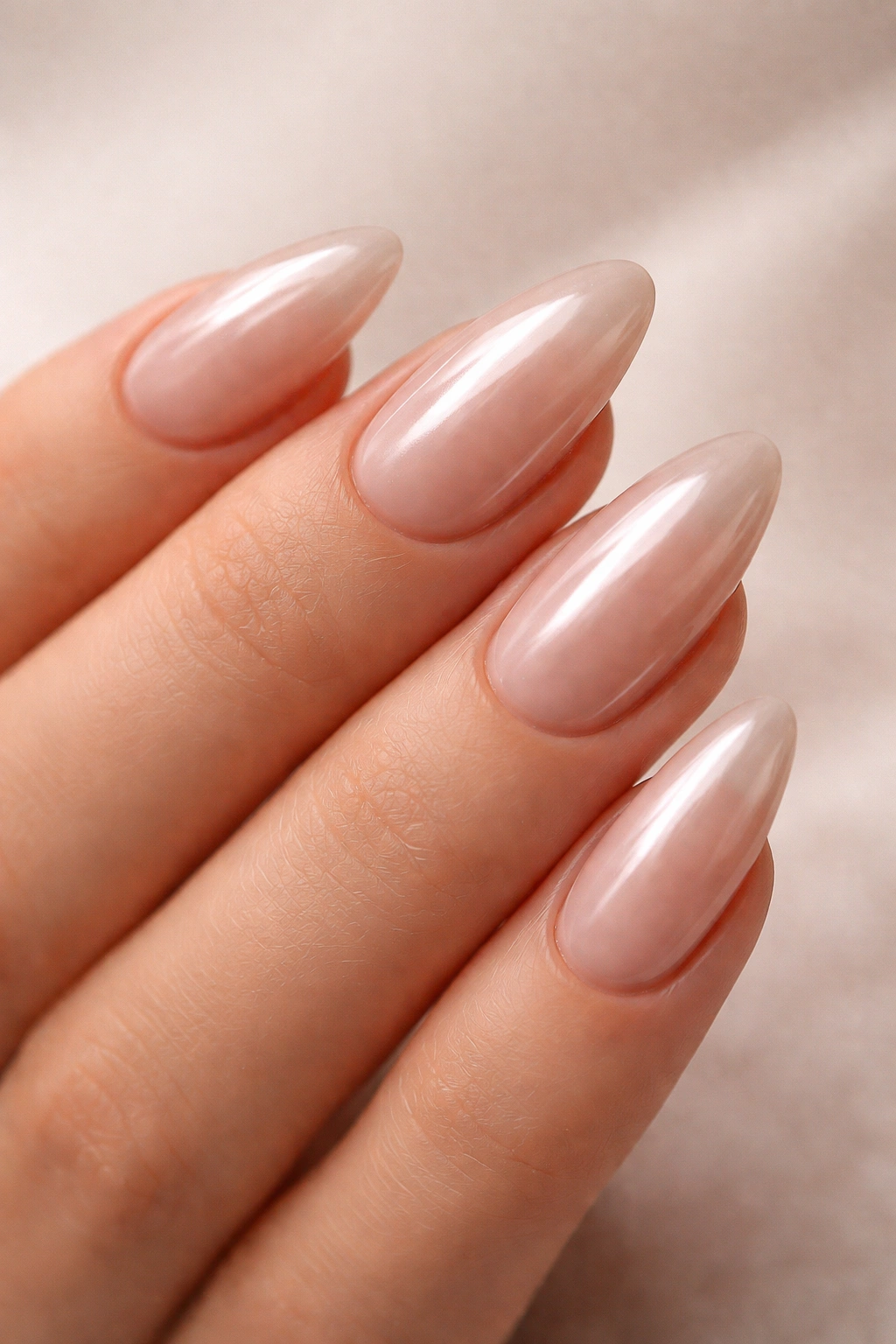 Close-up of nude almond nails with a subtle chrome finish on a beige base