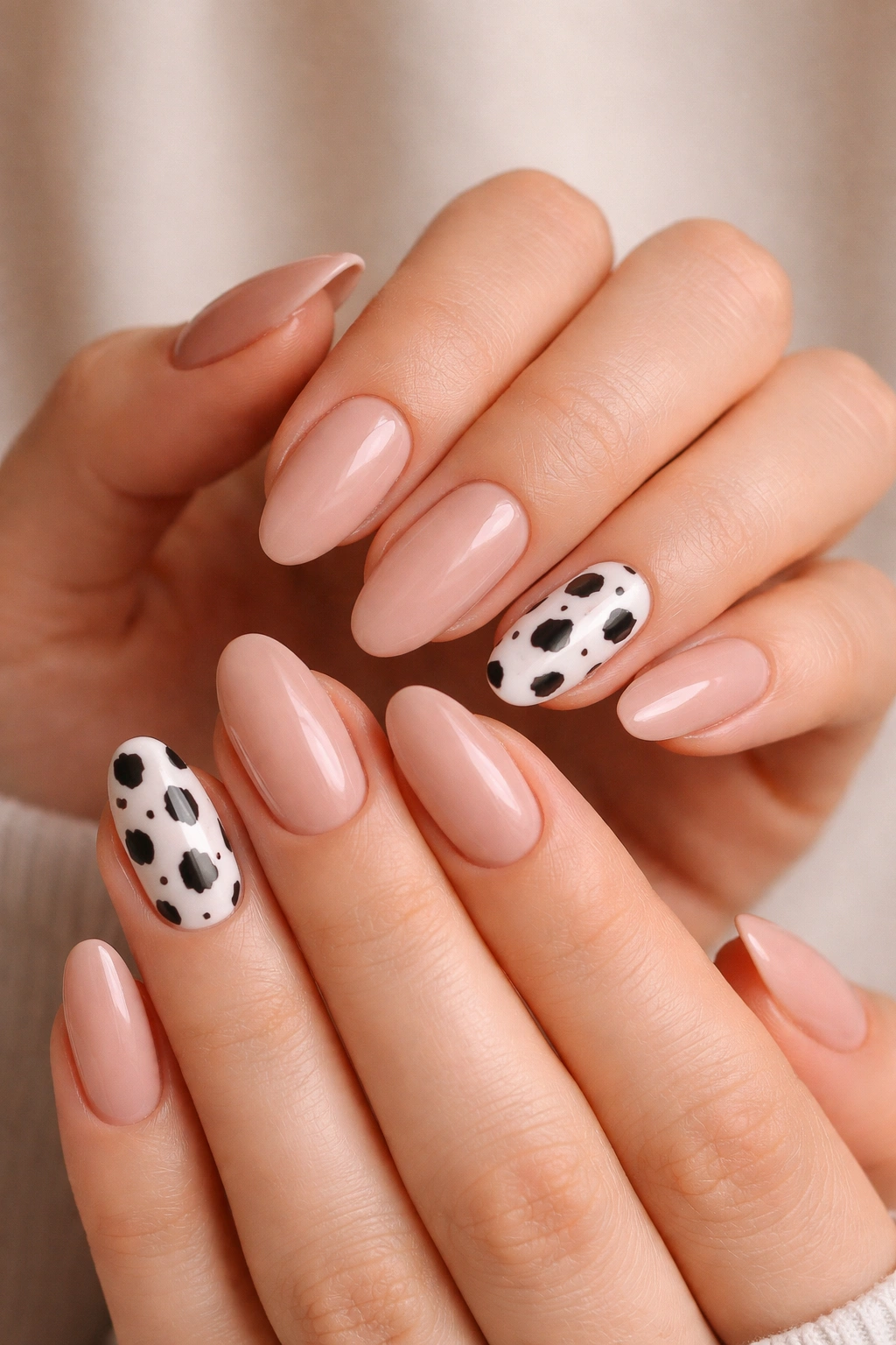 Close-up of nude almond nails with one cow-print nail per hand
