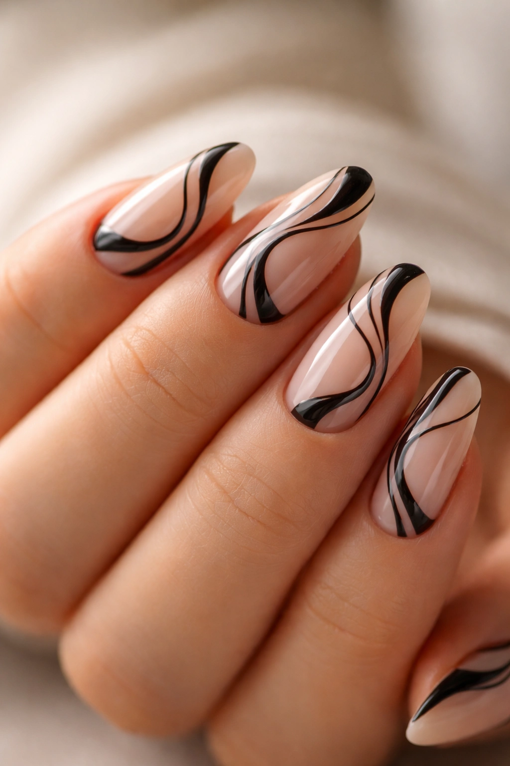 Close-up of short almond nails with nude base and black swirl nail art