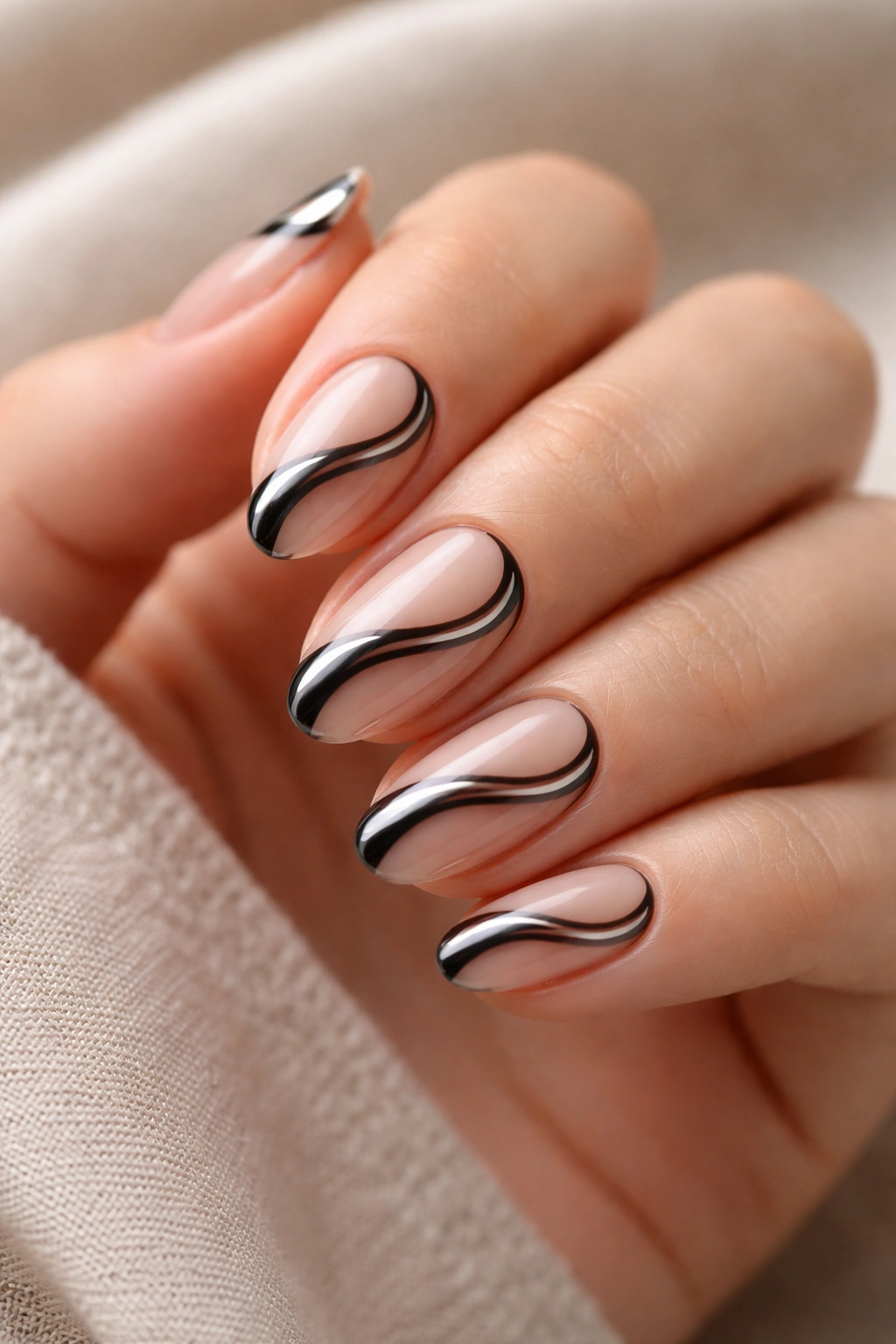 Close-up of short almond nails with black chrome swirls on a nude base