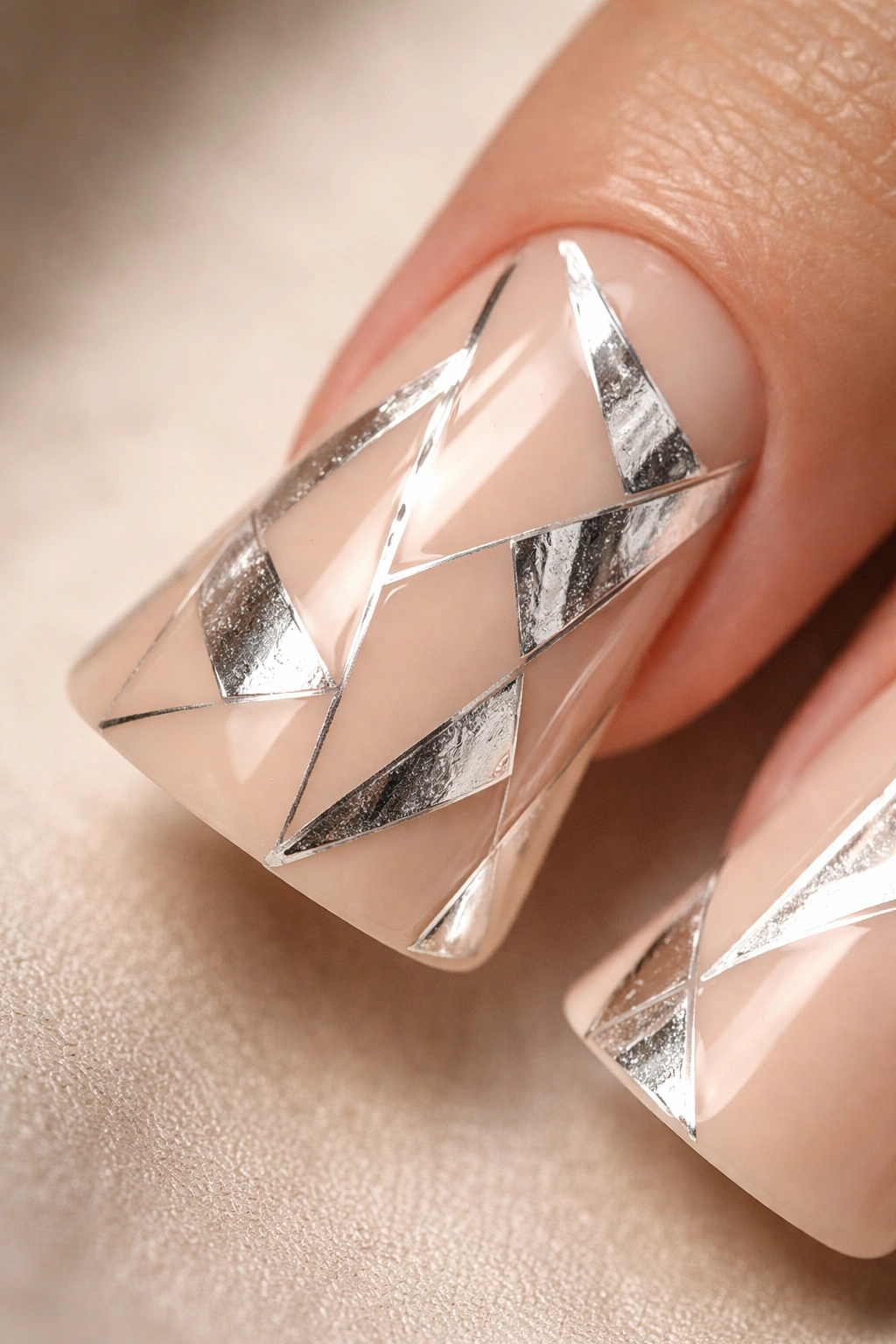 Duck nail with nude base and silver foil geometric shapes on a neutral background