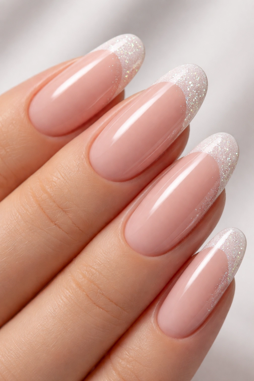 Close-up of nails with nude base and glittery white French tips on long round nails