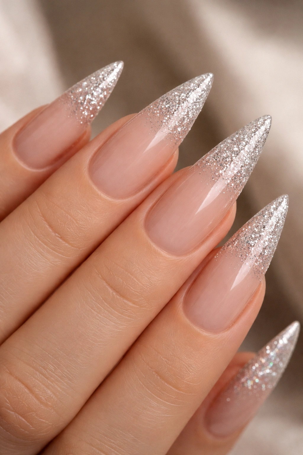 Close-up of nude base stiletto nails with glitter tips ombre