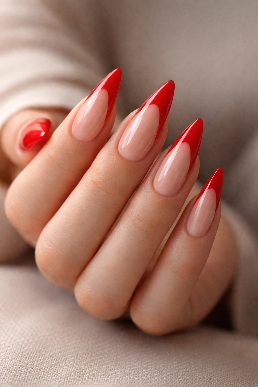 Nude-based stiletto nails with bright red tips against a soft neutral background