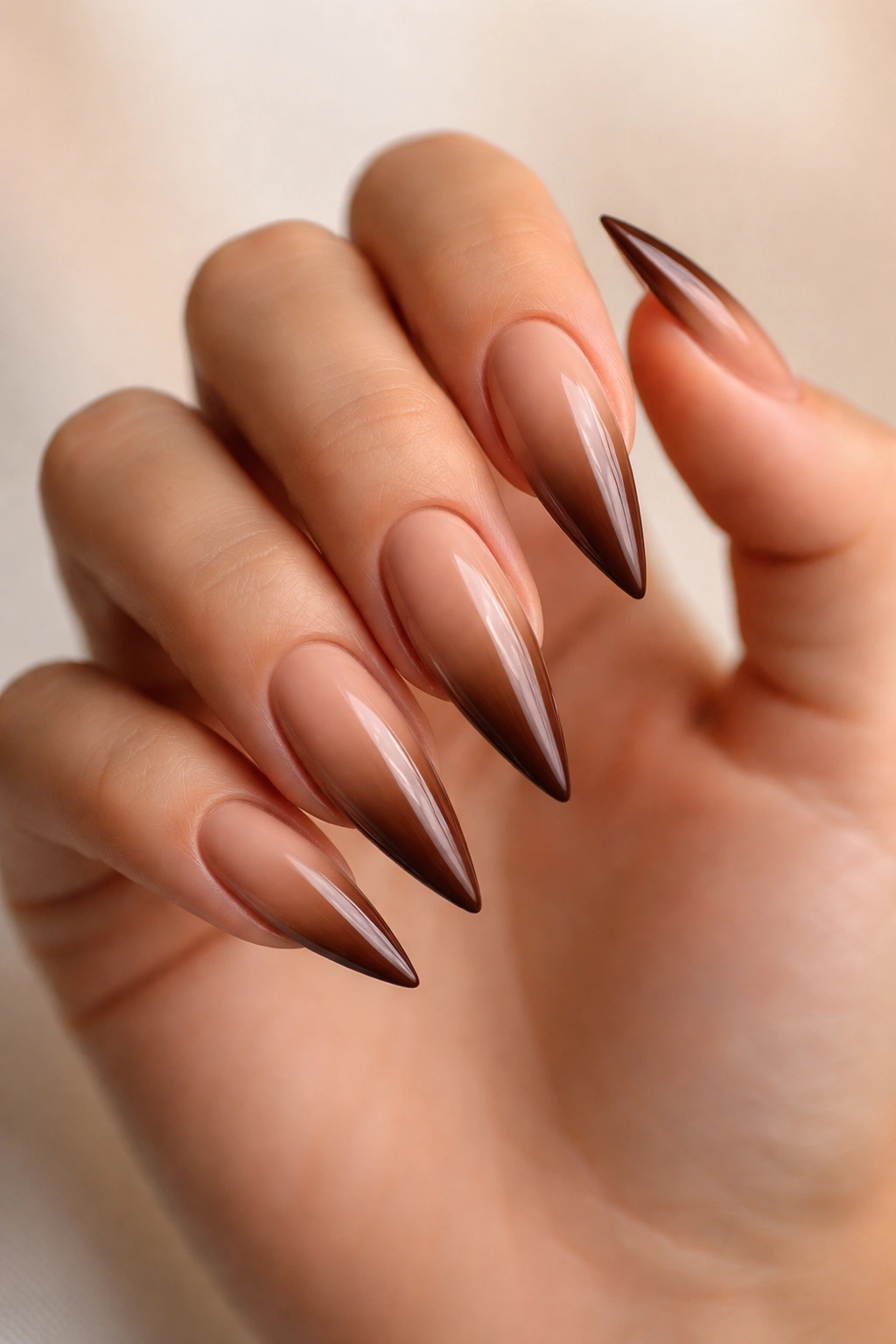 Nude to brown gradient stiletto nails on soft neutral backdrop