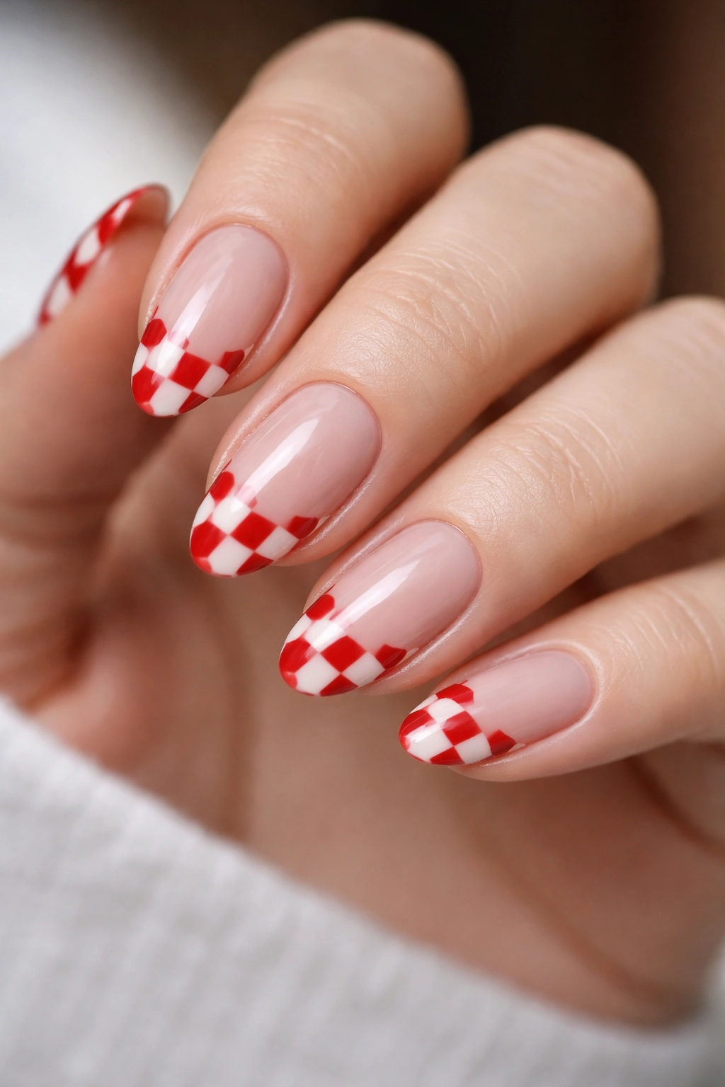 Close-up of almond nails with nude base and red checkerboard tips