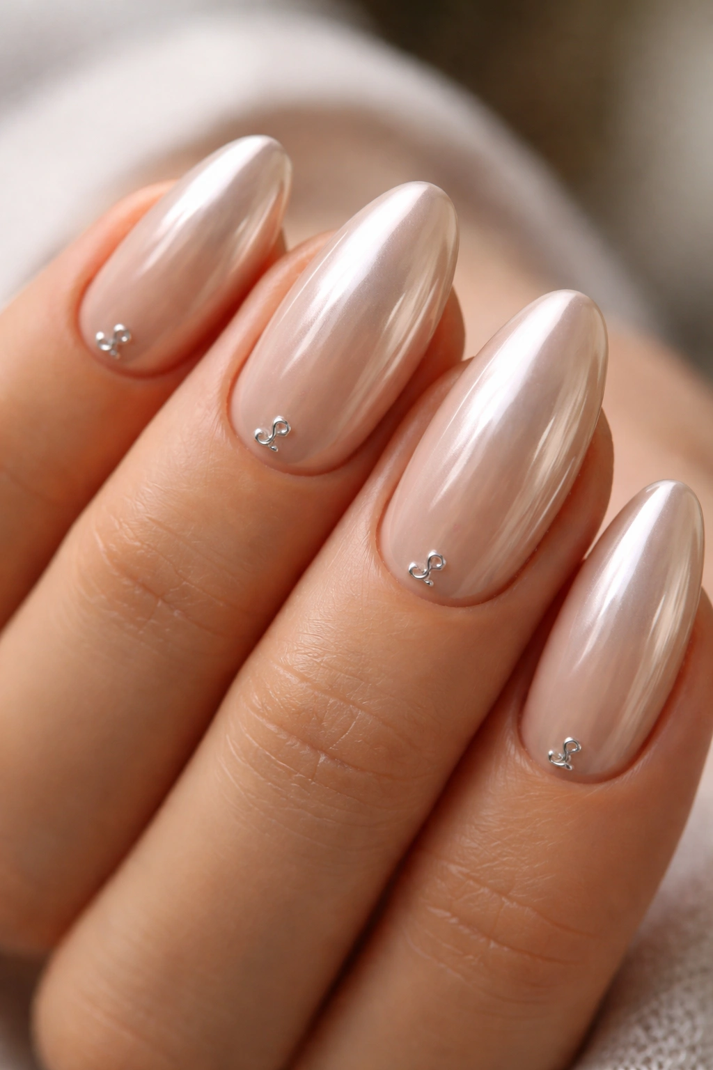 Close-up of nude chrome short almond nails with a silver initial-like mark